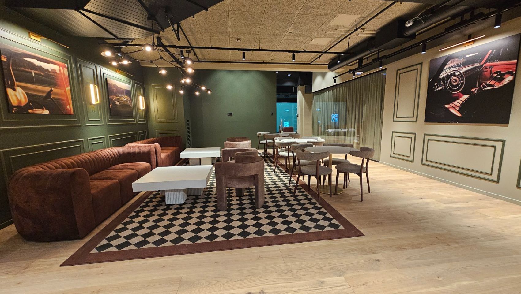 Loungeområde med brun sofa, hvite bord, sjakkrutet teppe og bilbilder på veggene