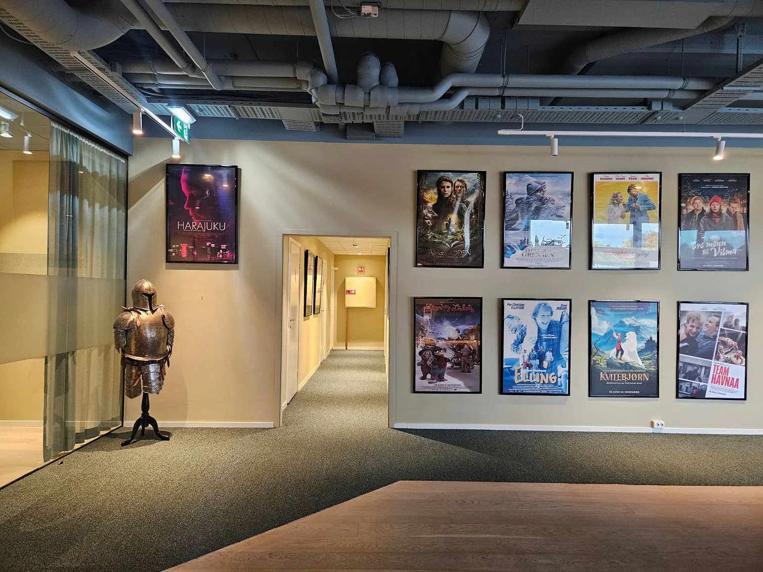 Innredet kontorområde med rustning på stativ og filmplakater på veggen langs en korridor.